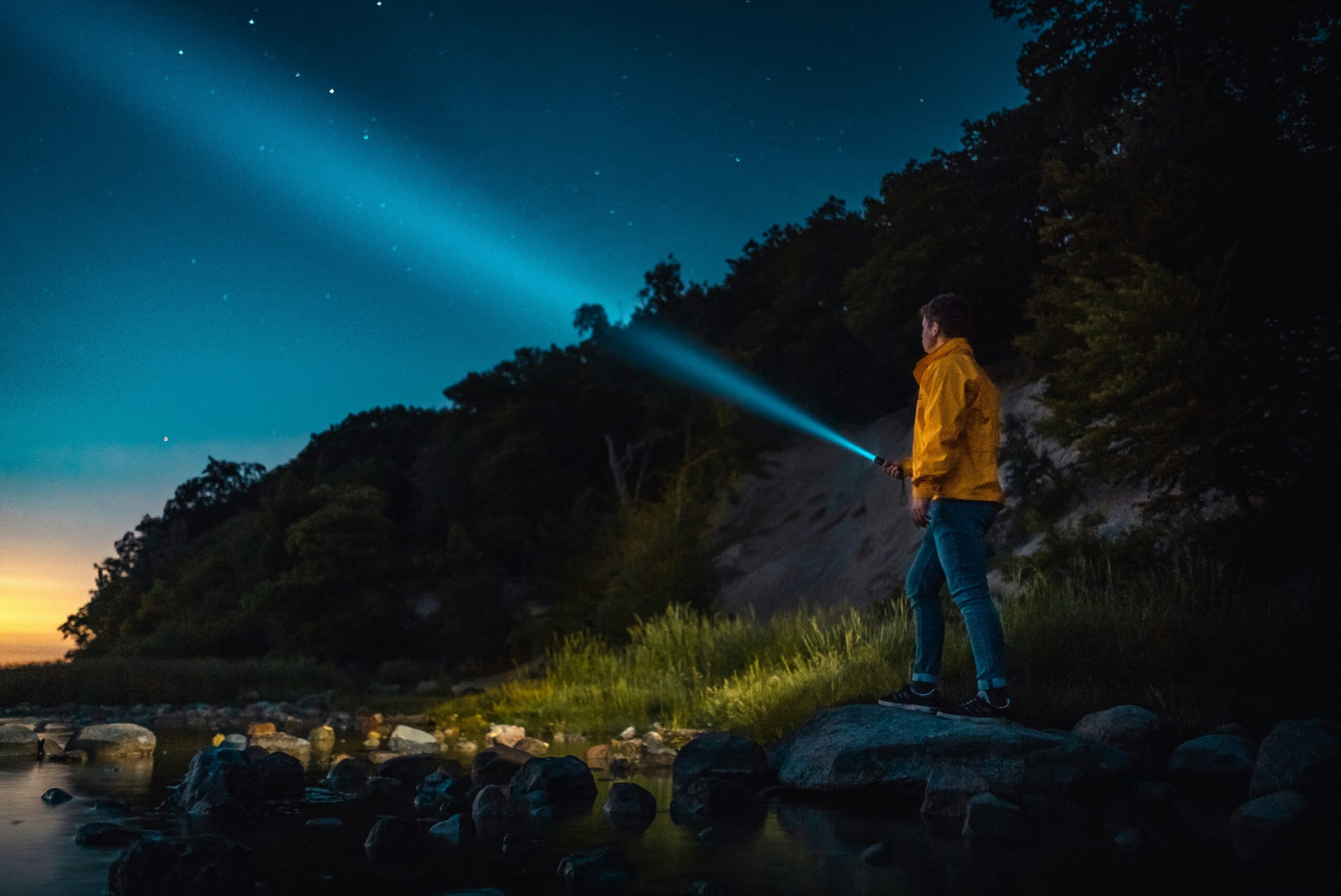 Explorador nocturno alumbrando con una linterna potente hacia los árboles junto al agua.